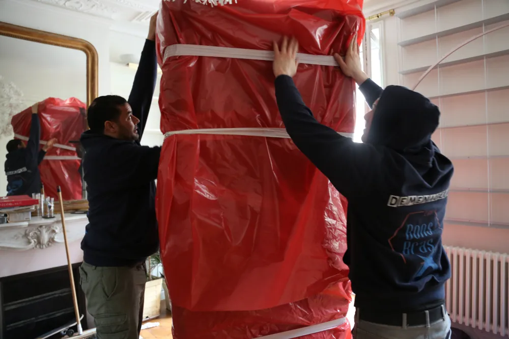 Deux déménageurs emballent un meuble dans uen housse de protection rouge